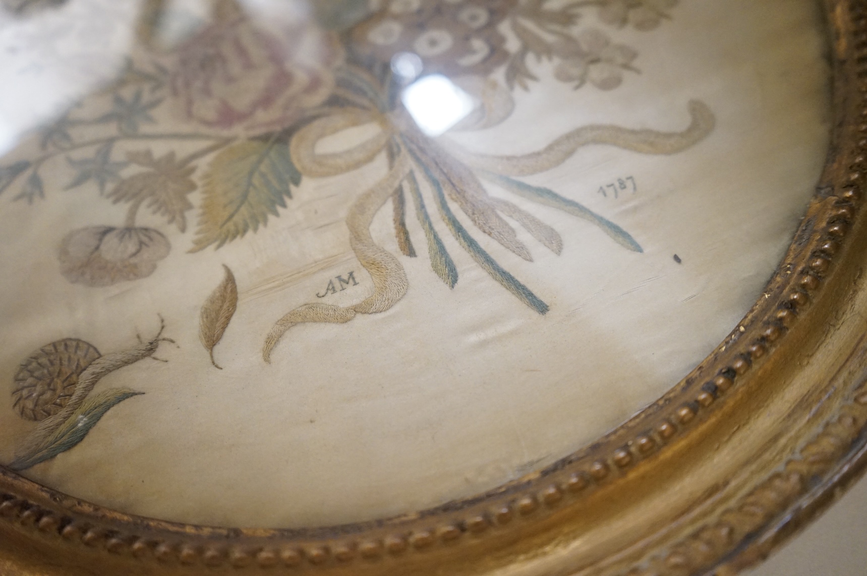 Two 18th century oval silkwork panels, one depicting flowers, monogrammed AM and dated 1787, together with a 19th century watercolour portrait of a lady, largest 42cm high